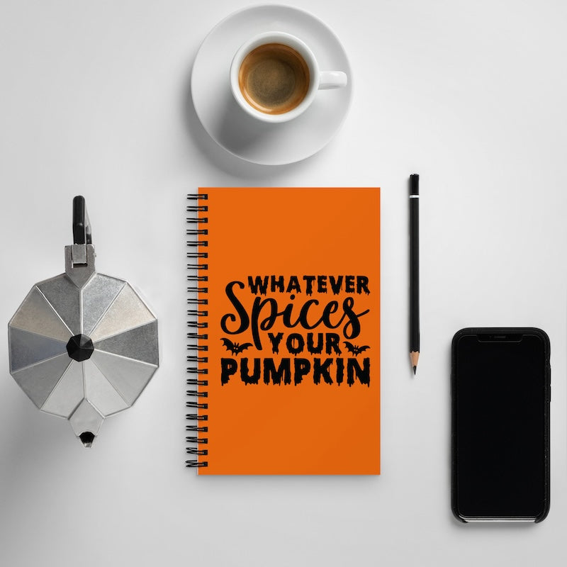 Orange notebook with 'Whatever Spices Your Pumpkin' text, coffee cup, pen, and phone on a light gray background