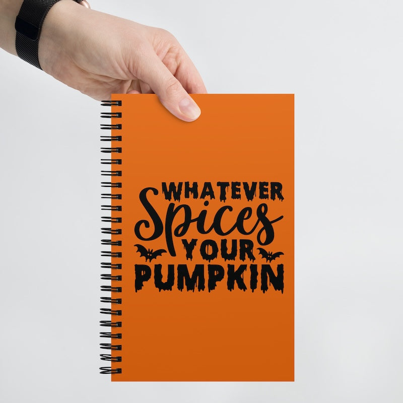 Orange notebook with 'Whatever Spices Your Pumpkin' text held by a hand on a light gray background