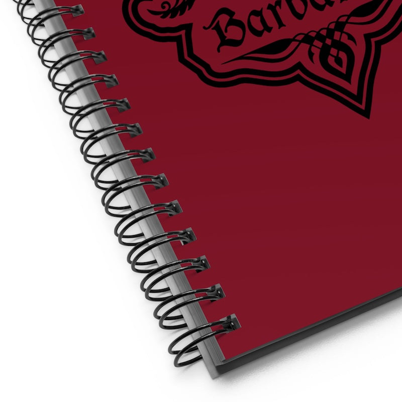 Red notebook with black spiral binding and decorative emblem on a white background