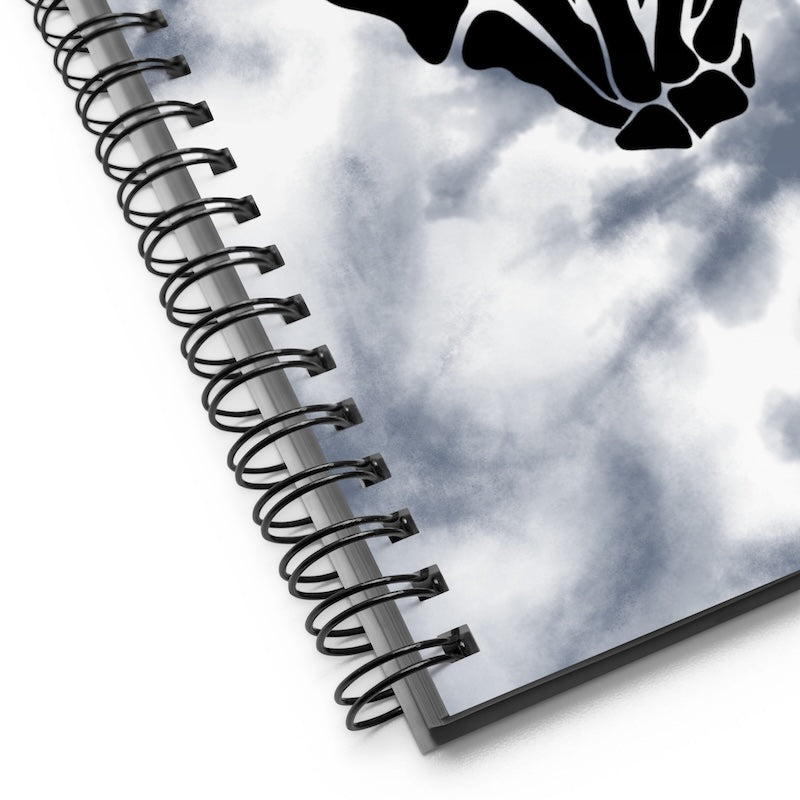 Spiral-bound notebook with a black and white abstract design on a cloudy sky background