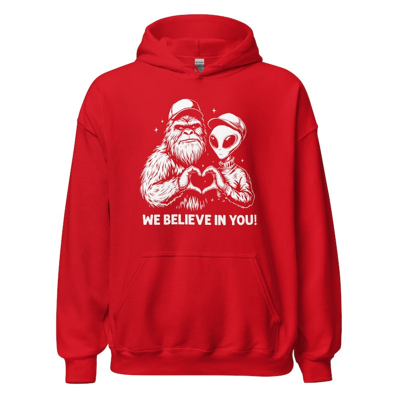 Red hoodie with a graphic of a bigfoot and alien holding hands and text 'WE BELIEVE IN YOU!' on a white background