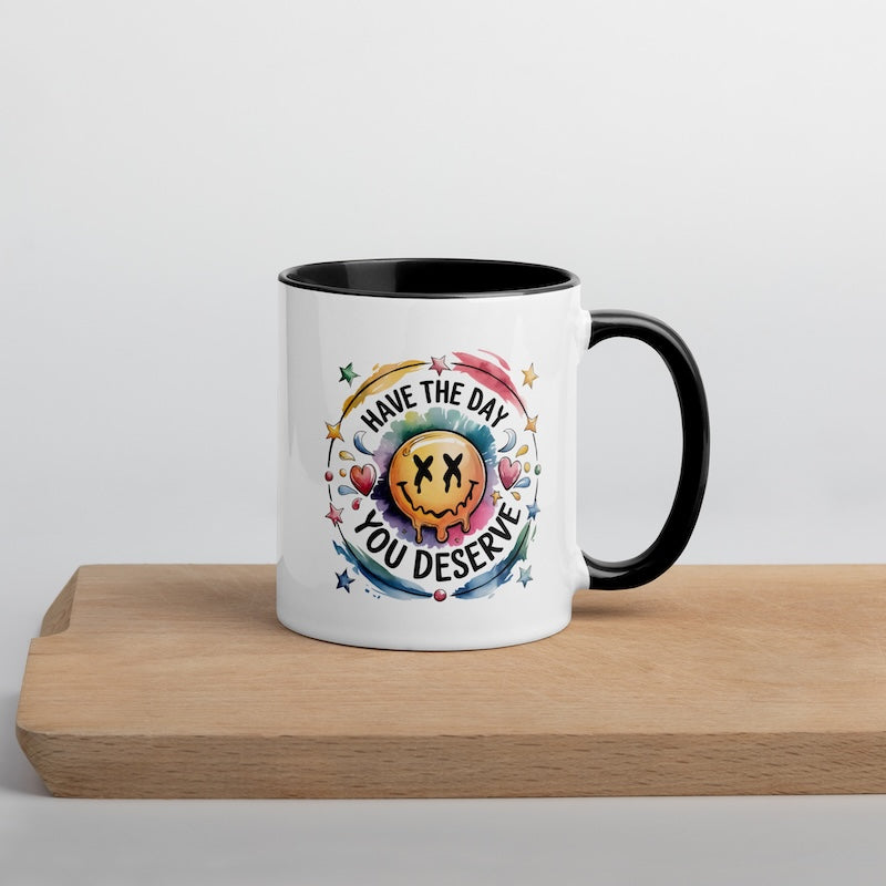 Mug with colorful design and text 'Have the day you deserve' on a wooden surface.