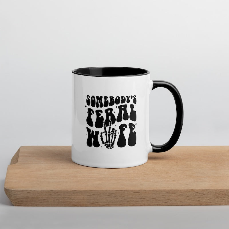 White mug with black interior and handle, featuring text and a skull design on a wooden surface.