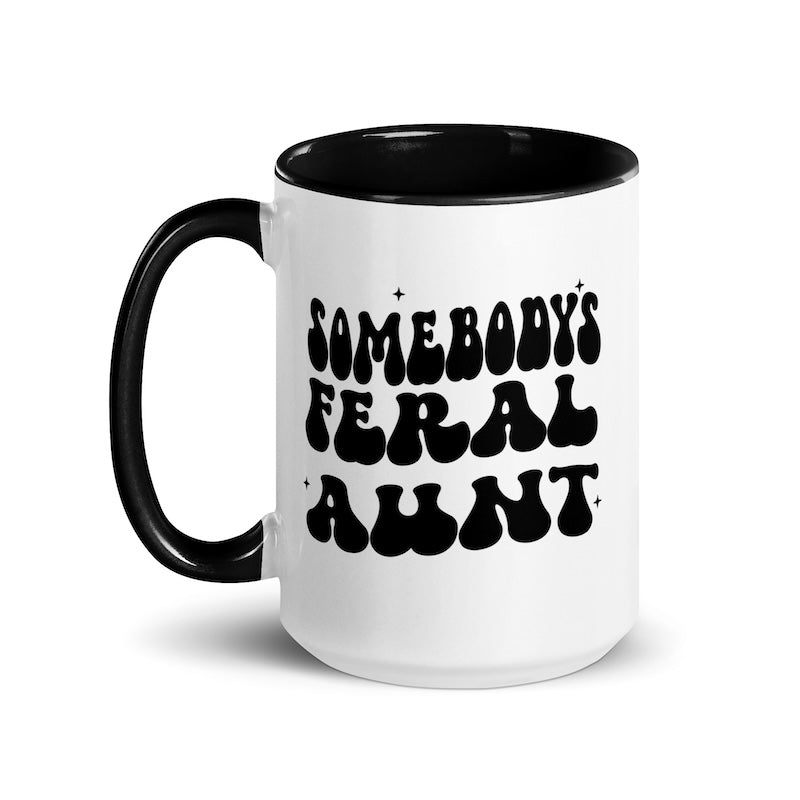 White mug with black interior and handle, featuring the text 'SOMEBODY'S FERAL AUNT' in black.