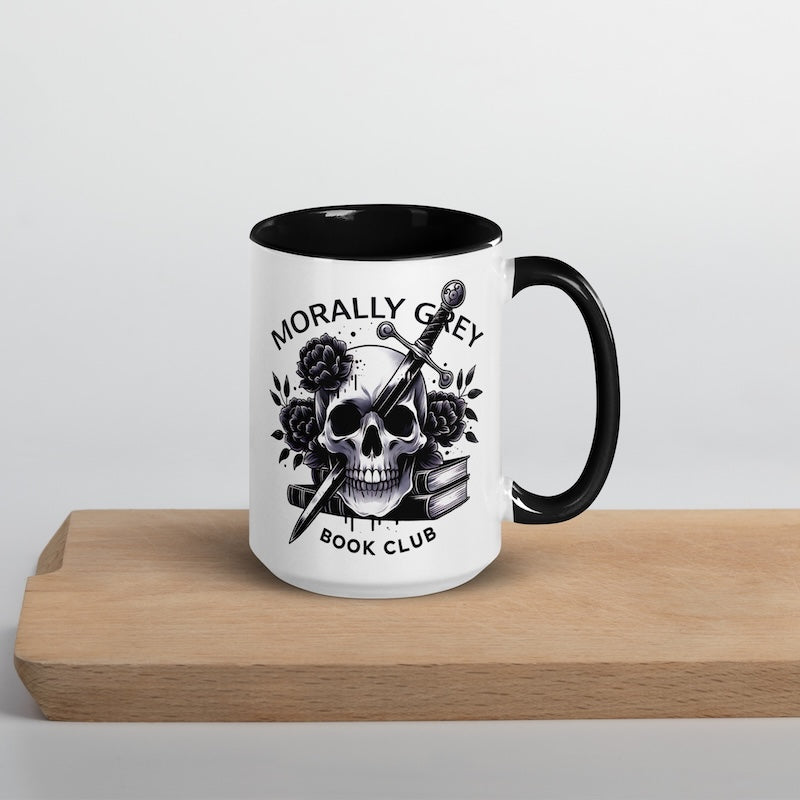 White mug with black interior and handle, featuring a skull and roses design, on a wooden surface.