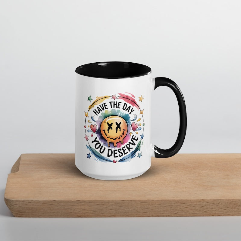 Mug with colorful design and text 'Have the day you deserve' on a wooden surface.