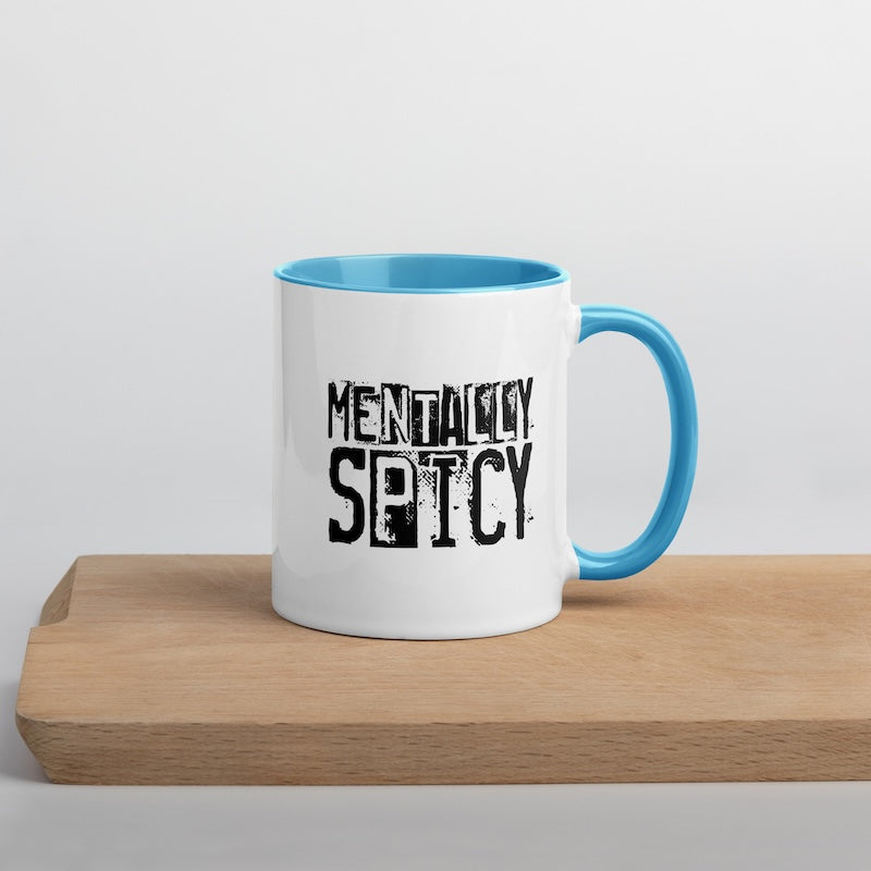 White mug with blue interior and handle on a wooden surface, featuring the text 'MENTALLY SPICY'.