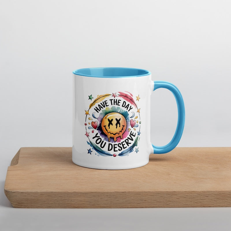 White mug with blue interior and handle, featuring a colorful design and text on a wooden surface.