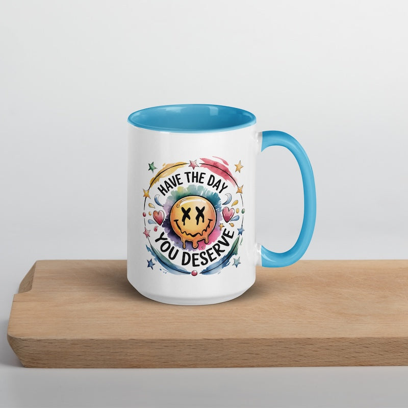 Mug with colorful design and text 'Have the day you deserve' on a wooden surface.
