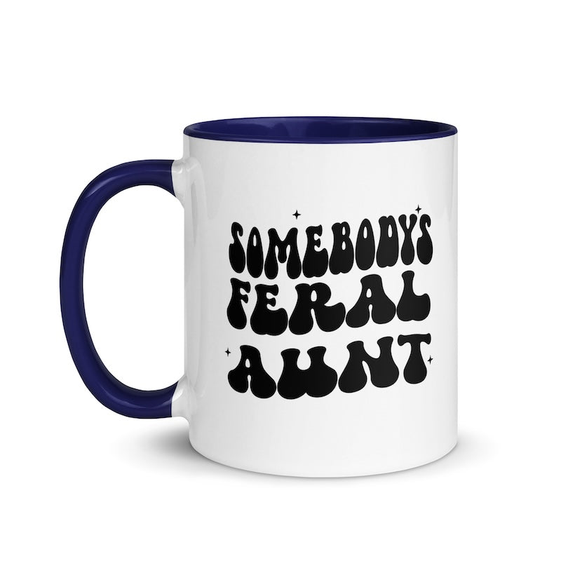 White mug with blue handle and interior, featuring the text 'SOMEBODY'S FERAL AUNT' in black.