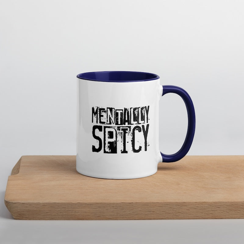 White mug with blue interior and handle, featuring 'MENTALLY SPICY' text on a wooden surface.