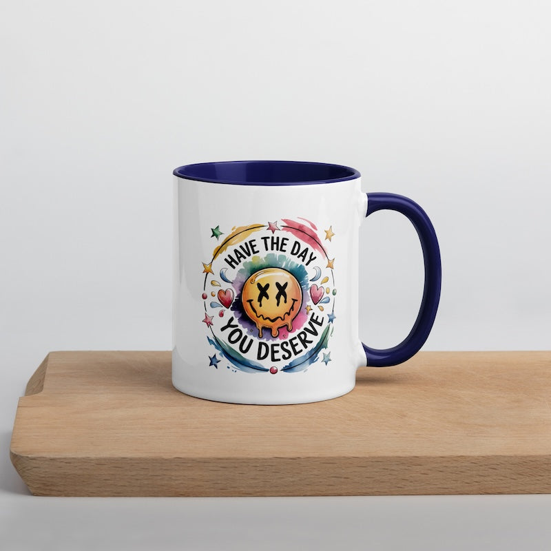 Mug with colorful design and text 'Have the day you deserve' on a wooden surface.