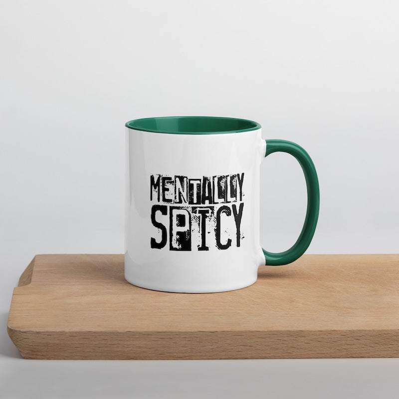 White mug with green interior and handle, featuring the text 'MENTALLY SPICY' on a wooden surface.
