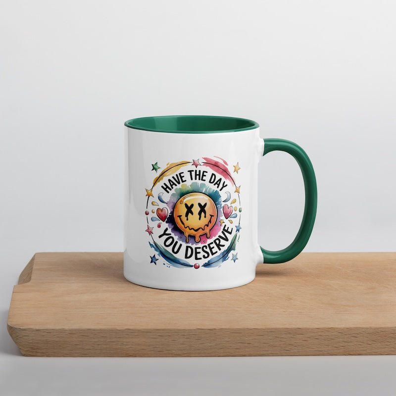 White mug with green interior and handle, featuring a colorful design and text on a wooden surface.
