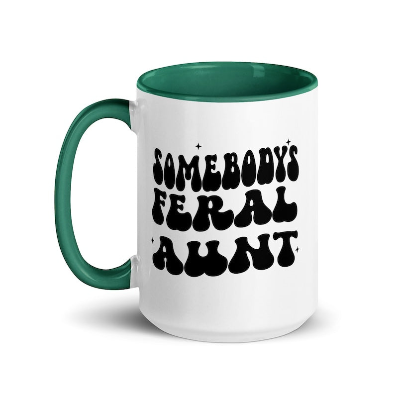 White mug with green handle and interior, featuring the text 'SOMEBODY'S FERAL AUNT' in black.