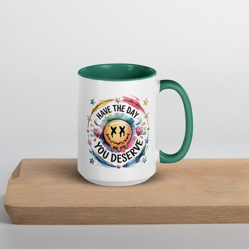 Mug with colorful design and text 'Have the day you deserve' on a wooden surface.