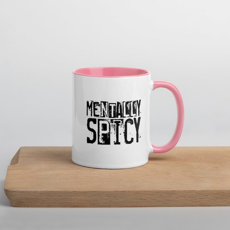 White mug with pink interior and handle, featuring the text 'MENTALLY SPICY' on a wooden surface.