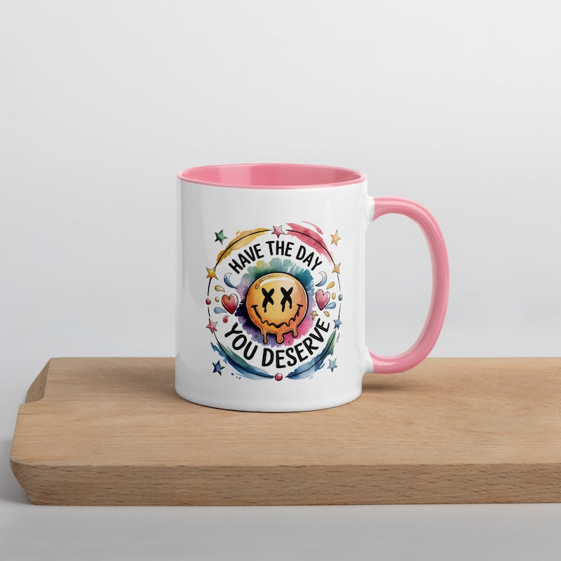 White mug with pink interior and handle, featuring a colorful design and text on a wooden surface.