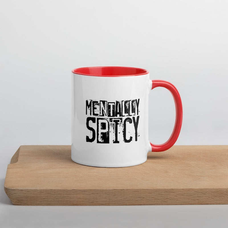 White mug with red interior and handle, featuring 'MENTALITY SPICY' text on a wooden surface.