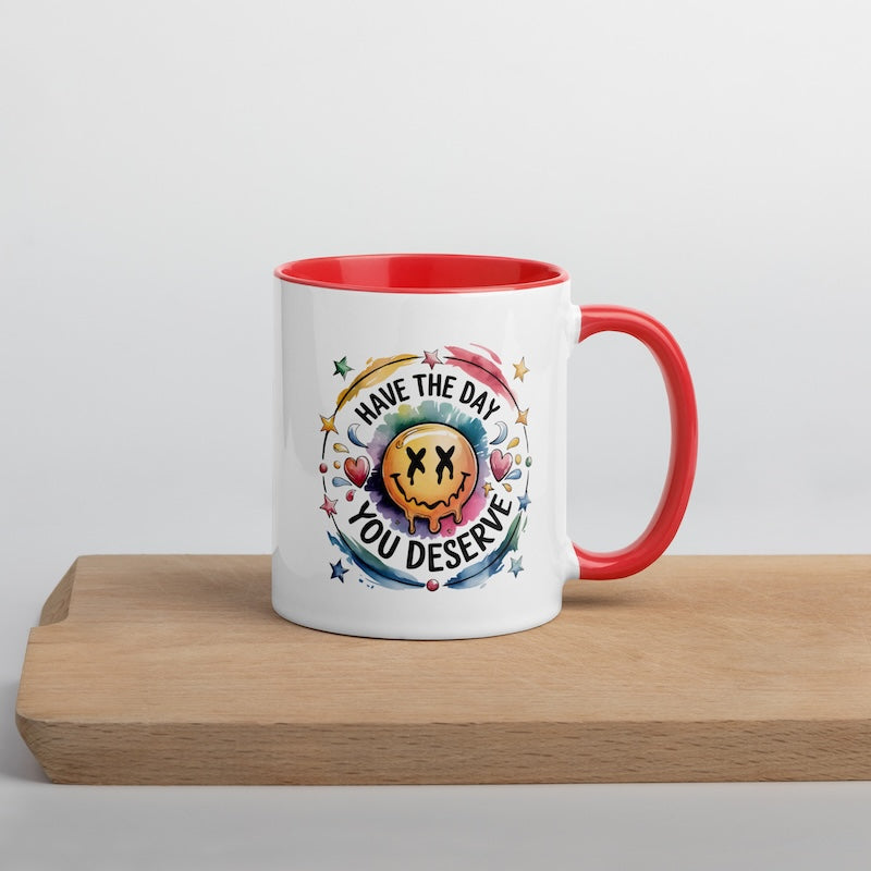Mug with red interior and handle on a wooden surface, featuring a colorful design and text.