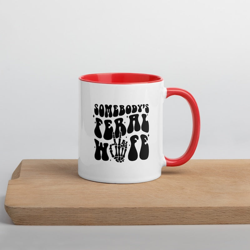 White mug with red interior and handle featuring black text on a wooden surface.