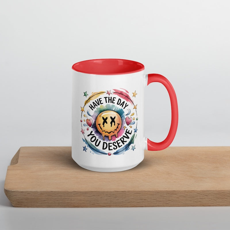 Mug with red interior and handle on a wooden surface, featuring a colorful design and text.