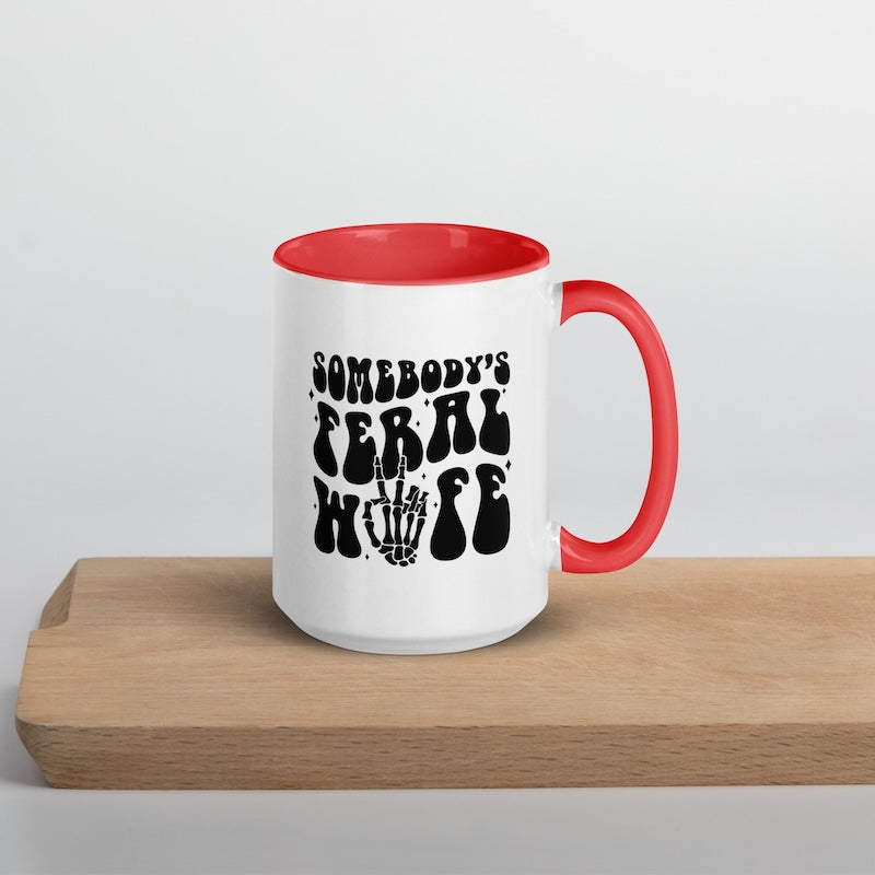 White mug with red interior and handle, featuring black text and skeleton hand graphic on a wooden surface.