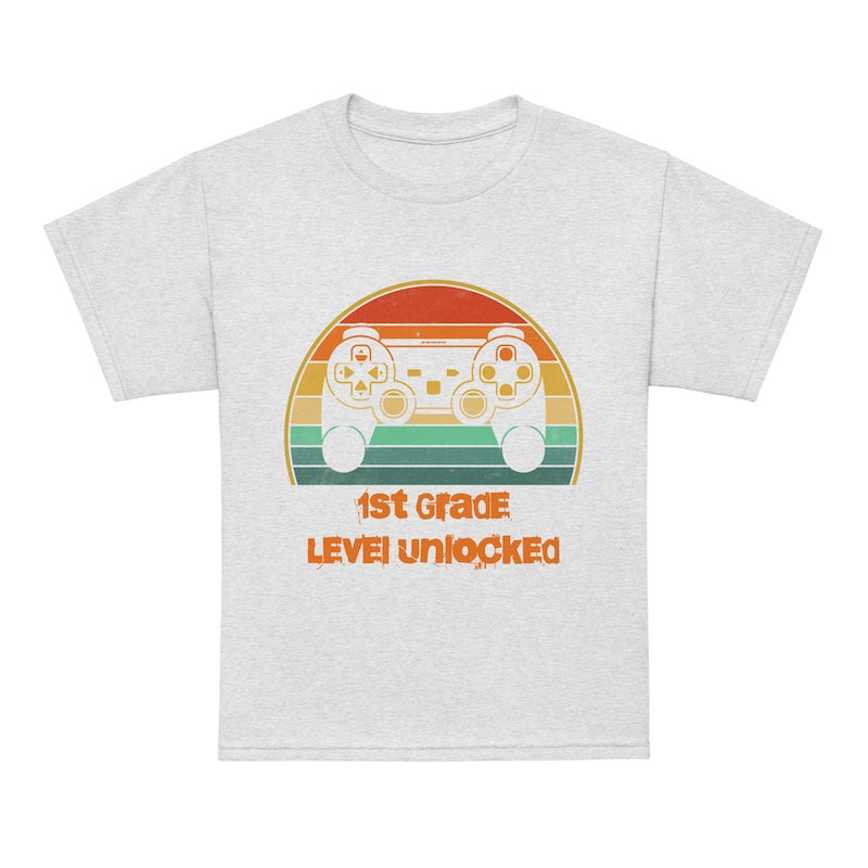 White t-shirt with gaming controller graphic and text '1st Grade Level Unlocked' on a white background