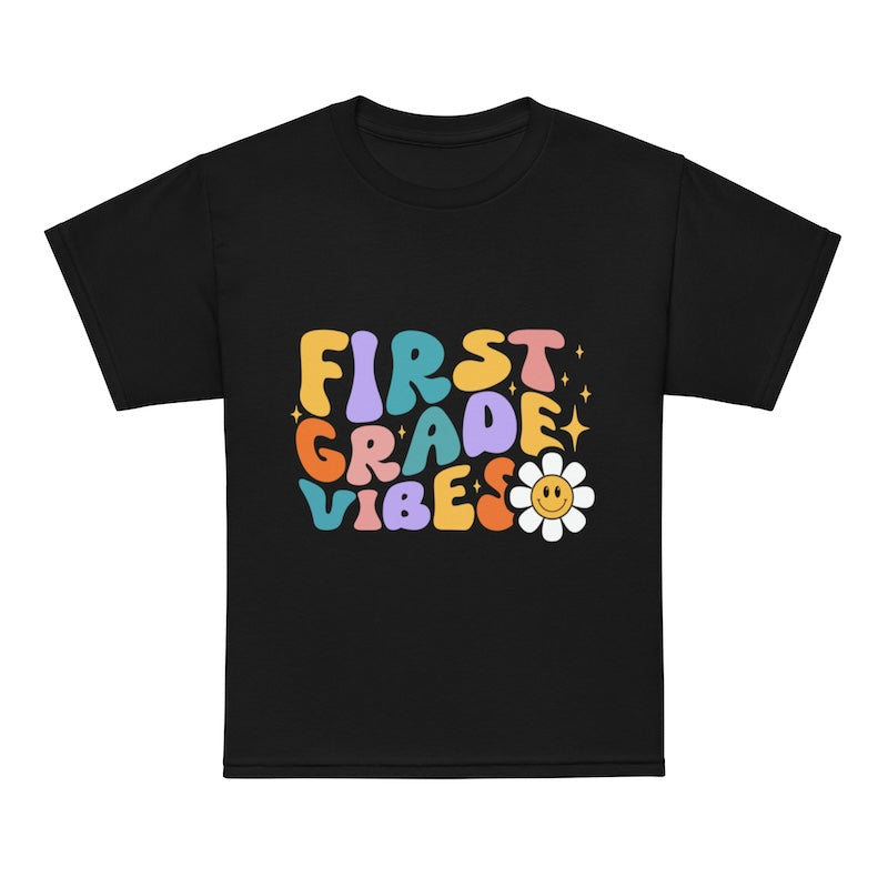 Black t-shirt with colorful 'First Grade Vibes' text and a flower graphic on a white background