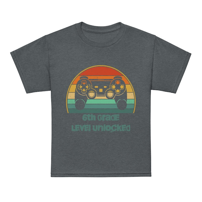 Gray t-shirt with a colorful graphic of game controllers and text '6th Grade Level Unlocked' on a white background.