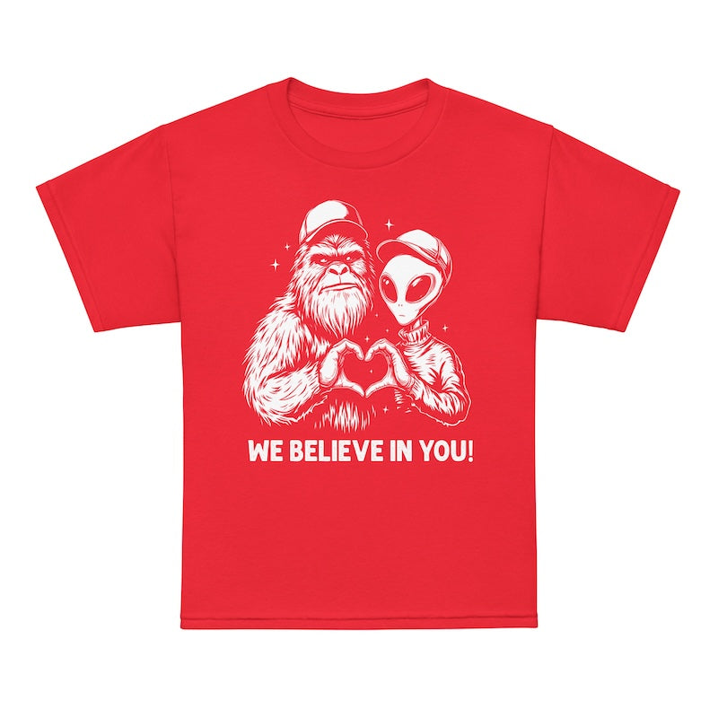 Red t-shirt with a graphic of a alien and a bigfoot holding hands and text 'WE BELIEVE IN YOU!' on a white background