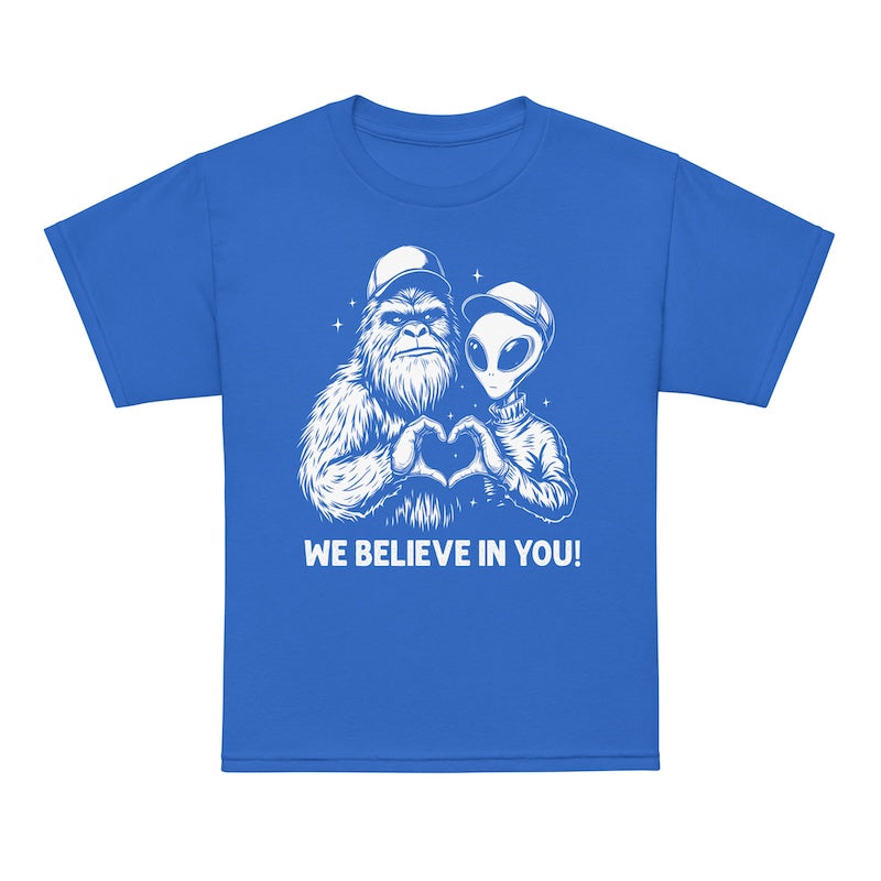 Blue t-shirt with a graphic of a alien and a bigfoot holding hands and 'We Believe In You!' text on a white background
